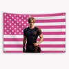 A man in a black shirt stands against a pink and white striped American flag banner.