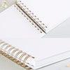 A spiral-bound white notebook with gold-toned metal rings lying on a light gray surface.