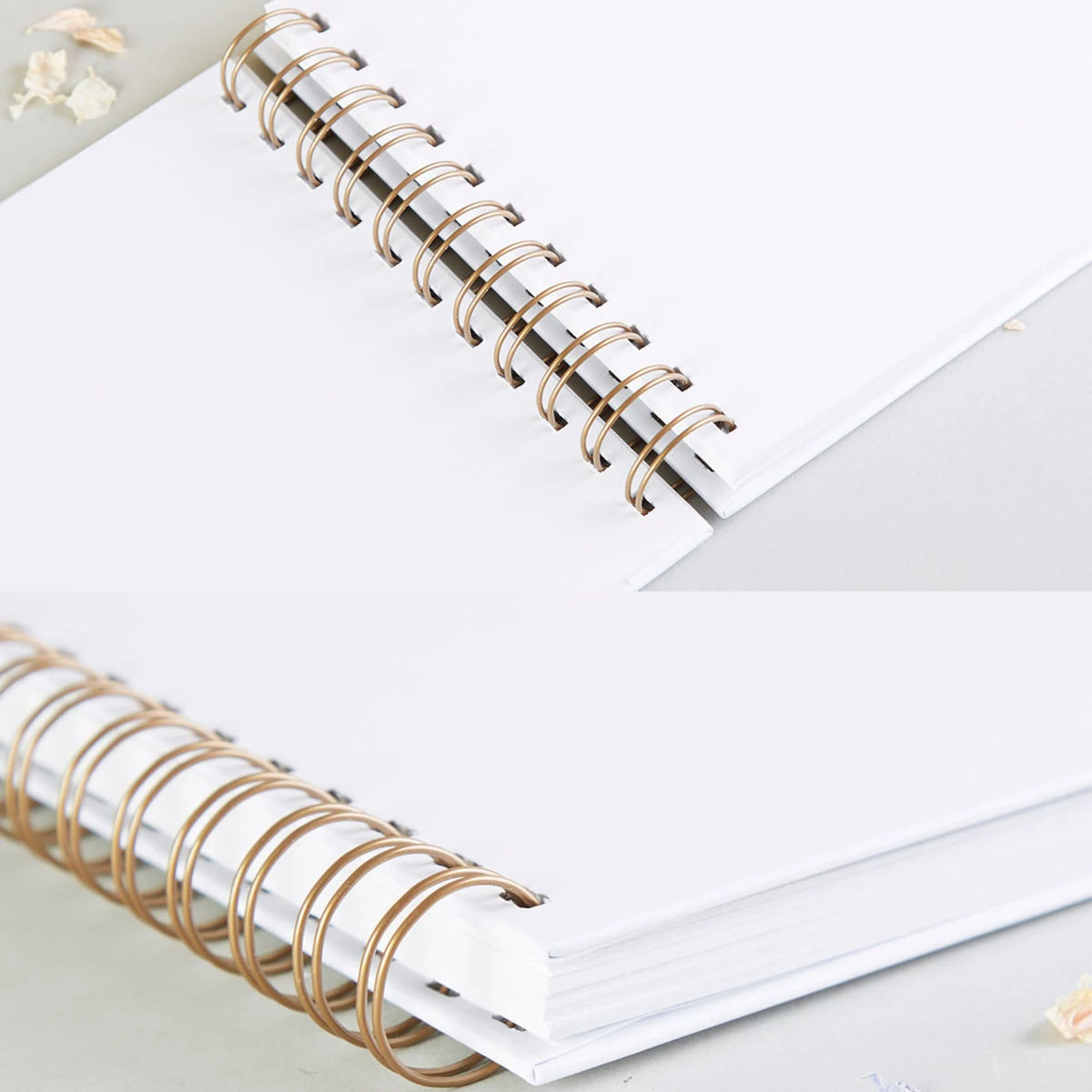 A spiral-bound white notebook with gold-toned metal rings lying on a light gray surface.