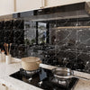 A modern kitchen setup featuring a black range hood above a marble countertop with a black induction cooktop and cookware.