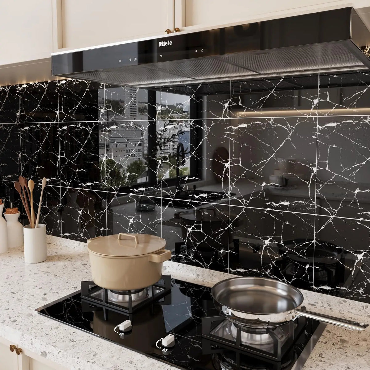 A modern kitchen setup featuring a black range hood above a marble countertop with a black induction cooktop and cookware.