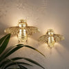 Handgefertigte goldene Bienenwandskulptur an der Wand mit sanftem Leuchten und grünen Blättern darunter.