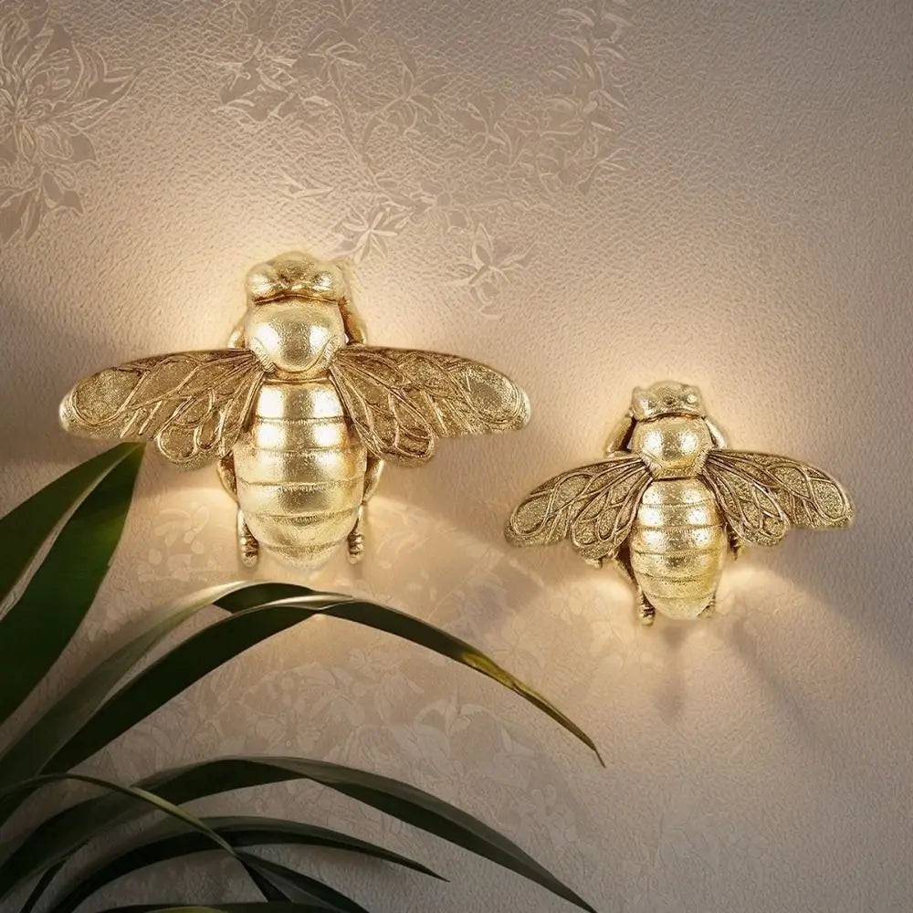 Handgefertigte goldene Bienenwandskulptur an der Wand mit sanftem Leuchten und grünen Blättern darunter.