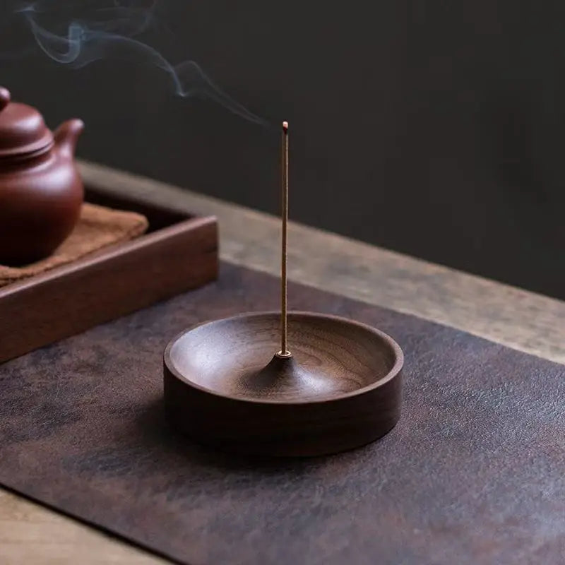A dark brown solid wood incense stick burner with a thin metal stick emitting smoke on a dark surface.