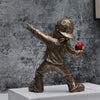 A bronze-colored resin sculpture of a figure throwing a red ball against a textured gray background.