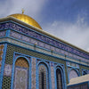 A close-up of an Islamic mosque dome and facade featuring intricate blue, gold, and green tilework.