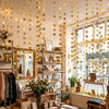 A display of shimmering gold and silver star paper garlands and bunting hanging in a bright shop setting.