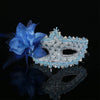A blue feather rhinestone masquerade mask resting on a reflective black surface.