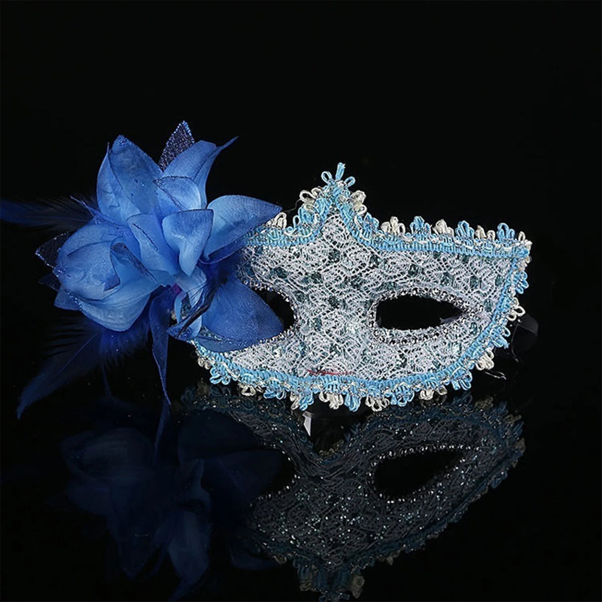 A blue feather rhinestone masquerade mask resting on a reflective black surface.
