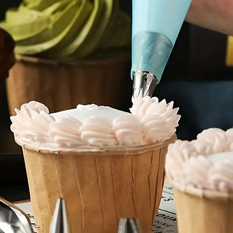 A hand is using a stainless steel piping nozzle to decorate a pink swirl of frosting on a paper cone.