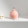 A pink ceramic mini vase with a rounded body and a small opening, shown on a white shelf.