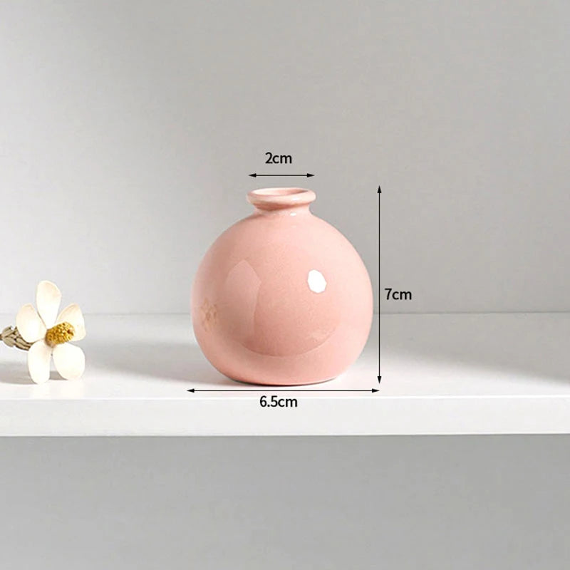 A pink ceramic mini vase with a rounded body and a small opening, shown on a white shelf.