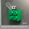 A green building block magnetic absorption box mounted on a wall, with a wire whisk and two small figurines nearby.