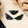 A set of black hand-carved obsidian bat figurines resting on a light beige surface next to animal bones.