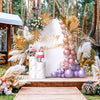 Arco de fondo floral y de hierba seca decorado con globos rosa, morado y beige para un evento.