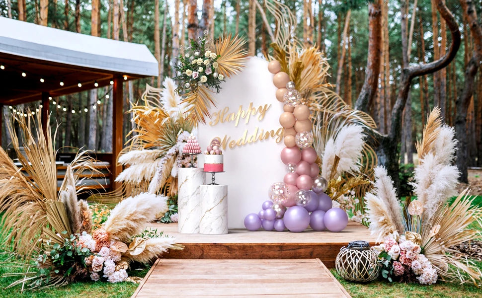 Arco de fondo floral y de hierba seca decorado con globos rosa, morado y beige para un evento.