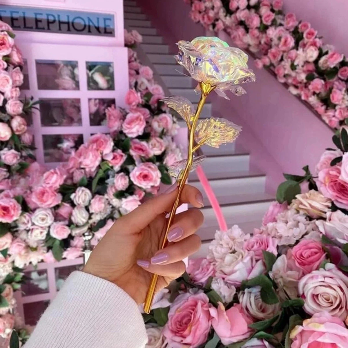 A hand holds a single golden crystal flower amidst a lush arrangement of pink and white artificial roses for home decor.