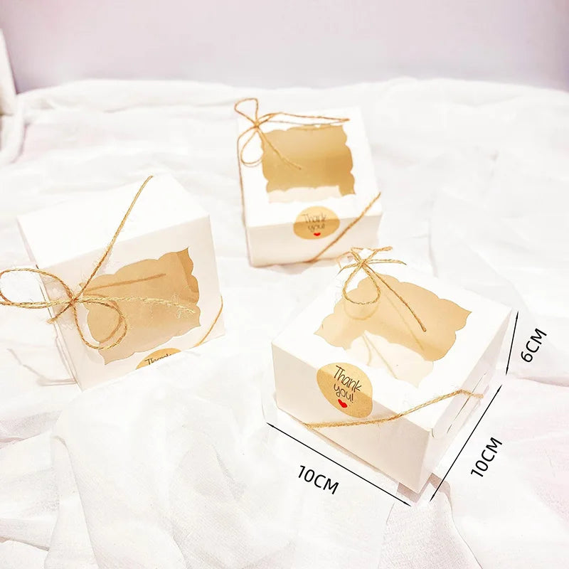 Three small kraft paper favor boxes tied with gold twine resting on white fabric.