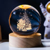 A dark blue crystal ball decoration featuring a laser engraved silhouette of a person standing next to a decorated Christmas 
