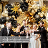 A group of people posing in front of an elegant black and gold balloon garland arch with starburst accents.