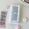 A white photo booth album featuring a clear plastic cover with a silver frame and pink accents, surrounded by star-shaped emb