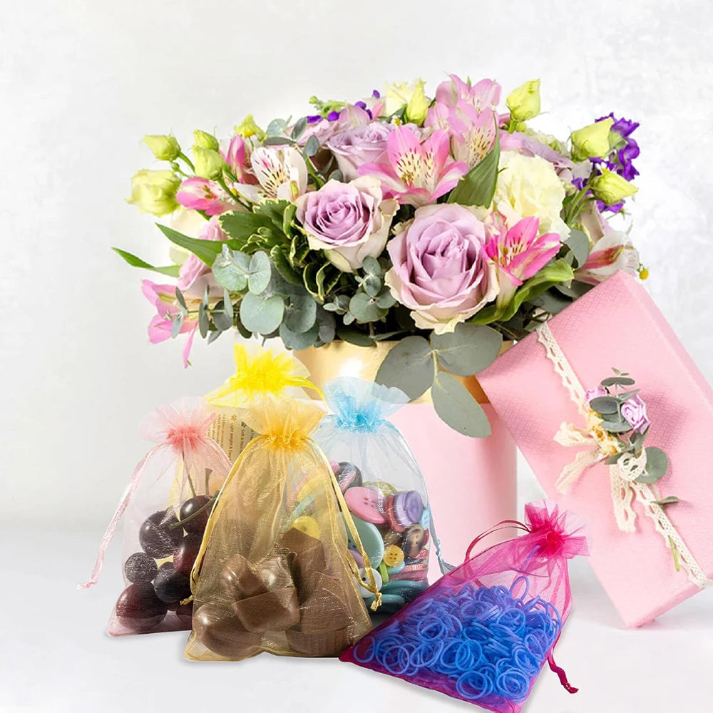 Elegant white and gold drawstring organza bags for gifts, weddings, and parties displayed with a floral arrangement