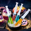 A collection of colorful party syringes with lids filled with liquids and ice cubes on brown paper.