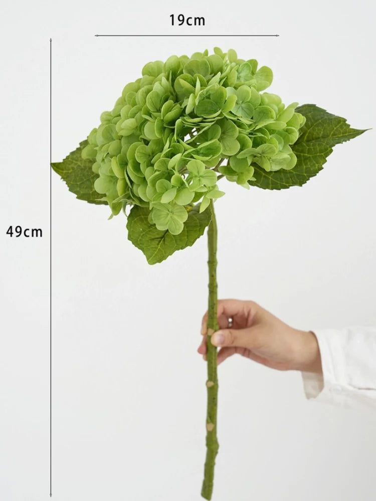 A green hydrangea silk flower branch with a stem and leaves is shown against a white background.