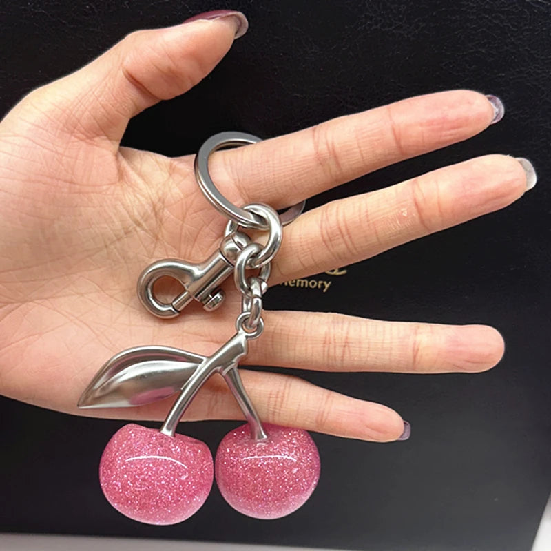 A hand holds a silver charm bag pendant featuring pink glittery cherry charms.