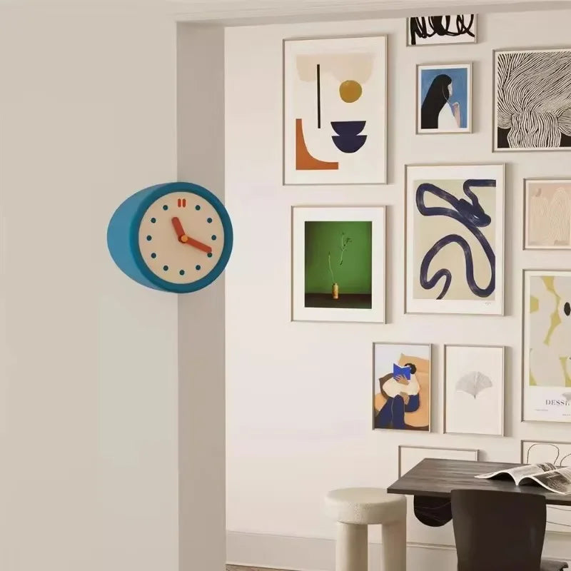 A modern resin wall clock with a blue face and wooden bezel is mounted on a light-colored wall above several framed abstract 