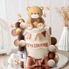 A tiered cake decorated with brown and gold spherical toppers and a bear figure.