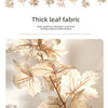 A display of thick leaf fabric garlands featuring realistic autumn maple leaves in shades of orange, green, and beige.