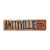 A rustic, weathered metal sign with the text AMITYVILLE and an arrow pointing to the right.