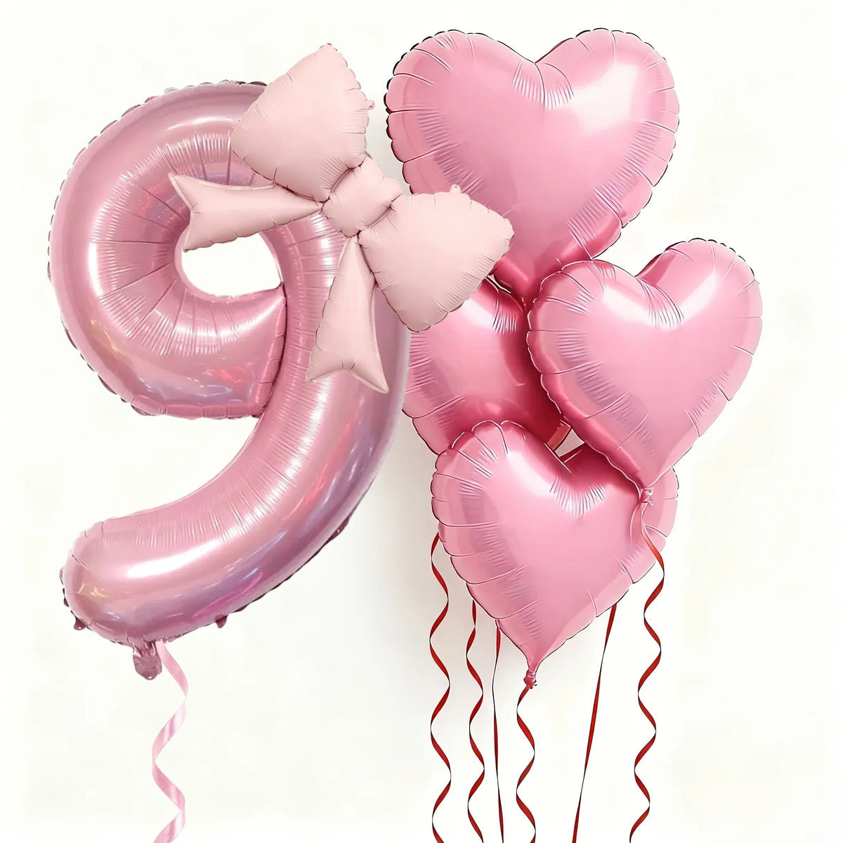Pink foil balloons shaped like the number 9 and heart, tied with pink bows, for party decoration.