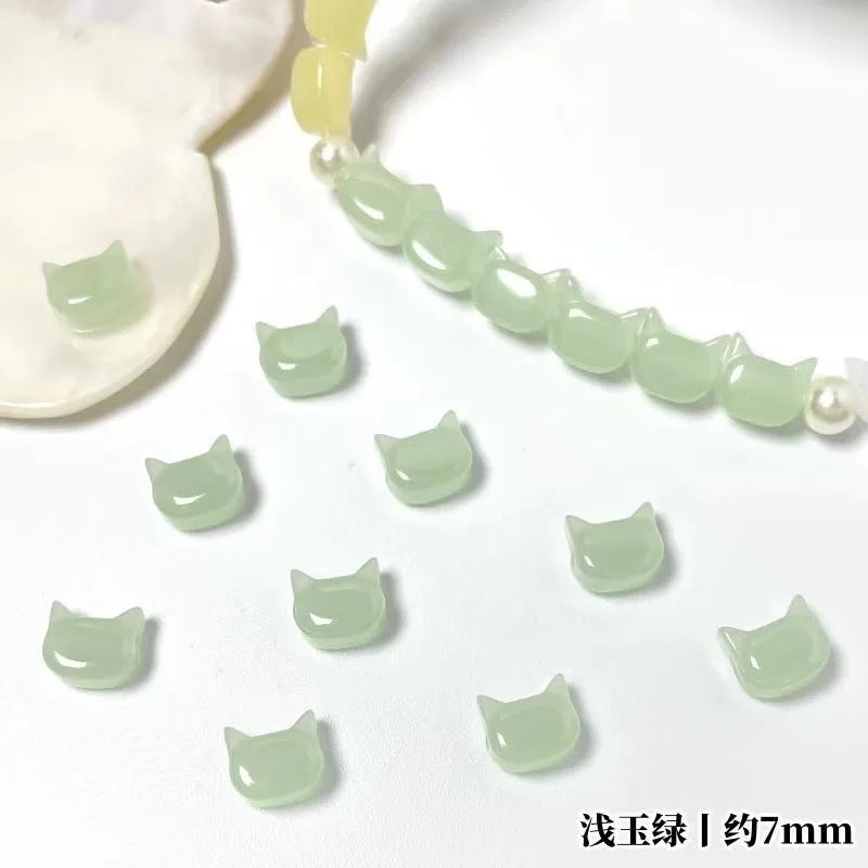 A string of light green cat head glass beads for jewelry making, with a white bead visible in the background.