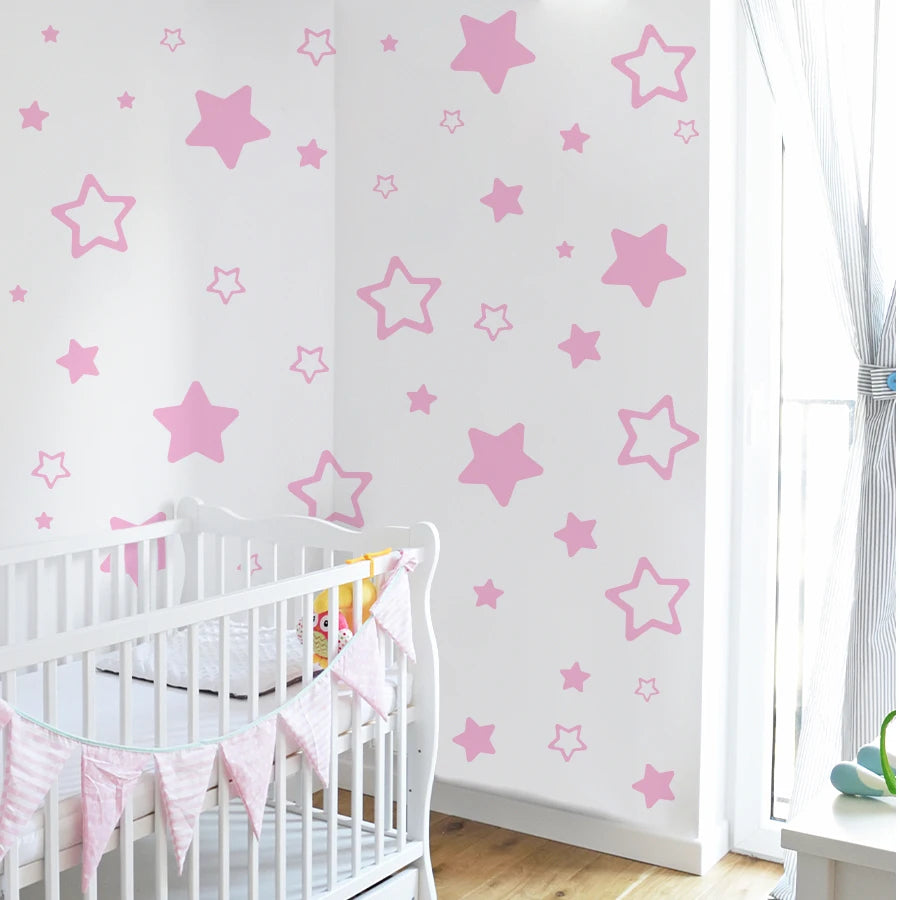 Pink star vinyl wall decal featuring various sized stars on a white wall with a crib in the foreground