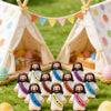 A collection of mini rubber Jesus figurines in various colors are displayed outdoors on a grassy field with Easter decoration