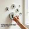 A hand is placing a silver flat hemisphere disco ball wall decor piece onto a white wall.