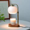 A brass aromatherapy wax melting lamp with a white globe light and a glass candle sits on a wooden base.