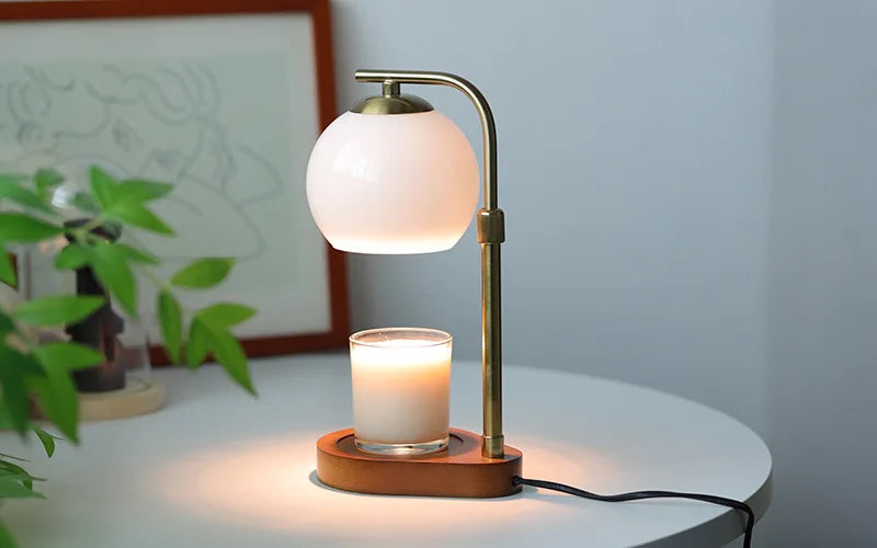 A brass aromatherapy wax melting lamp with a white globe light and a glass candle sits on a wooden base.