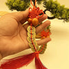 A hand holds a traditional Chinese knot pendant featuring an orange thread, wooden gourd, and stacked copper coins.