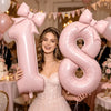 A young woman holds a large pink foil number balloon shaped like the number 18 with a bow.