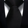 A close-up shot of a black silk necktie tied in a simple knot against a black suit jacket.