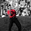 A man in a red shirt is swinging a golf club during a tournament, captured in black and white.
