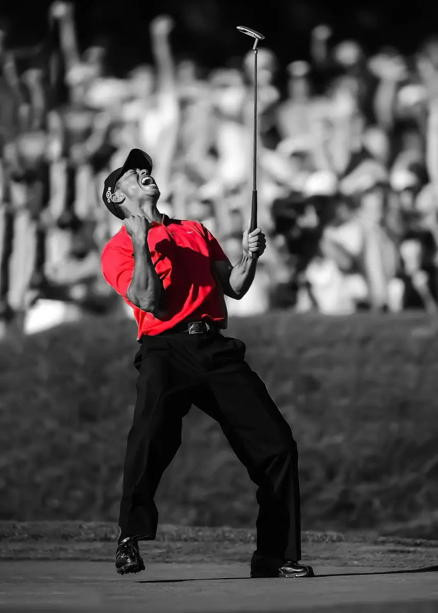 A man in a red shirt is swinging a golf club during a tournament, captured in black and white.