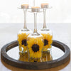 Three glass candle holders with yellow flowers and white tealight candles displayed on a dark wooden tray.