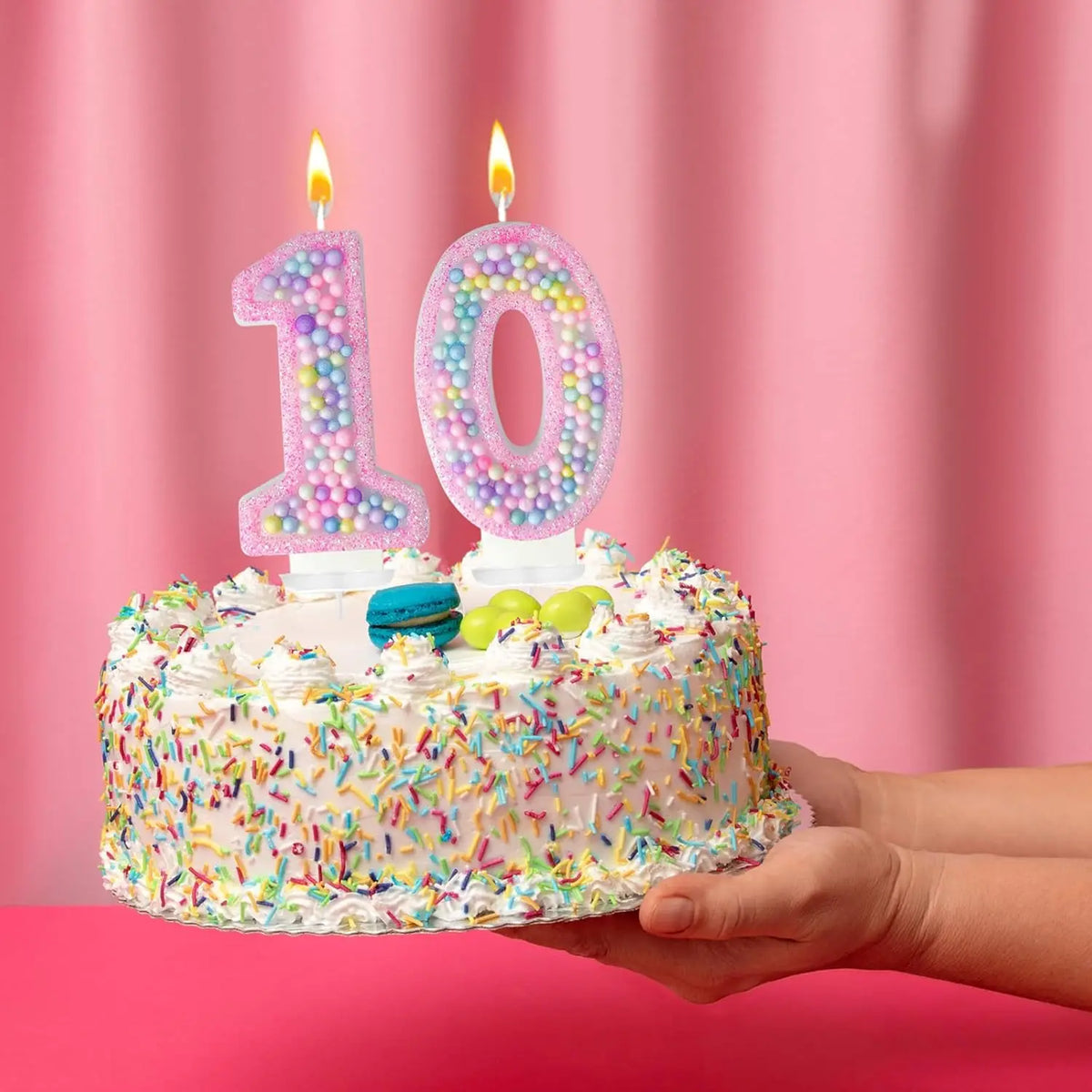 A pink birthday cake decorated with large number candles spelling '10' and colorful sprinkles.