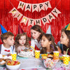 A birthday party setup featuring a red curtain backdrop with a banner, cake, and colorful decorations.