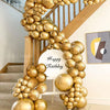 A golden balloon garland decoration is displayed on a wooden staircase railing.