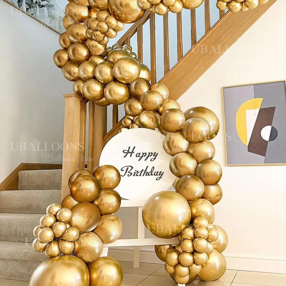 A golden balloon garland decoration is displayed on a wooden staircase railing.